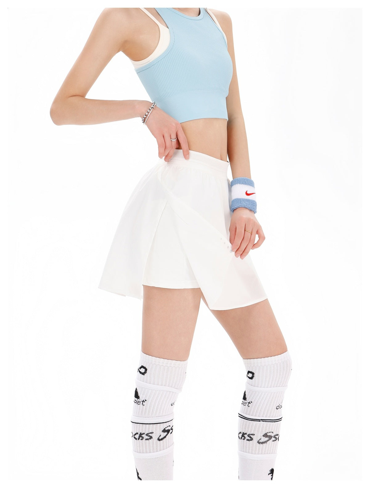 Front view of a model wearing a white wrap-style tennis skirt, opened to show the built-in shorts.