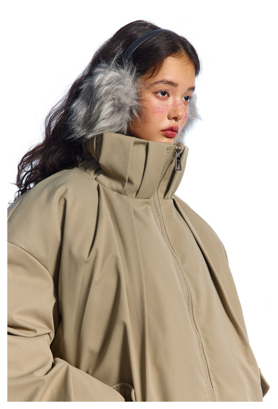 Close-up of a taupe jacket's high collar, front zipper, and gray fur-trimmed hood worn by a model.