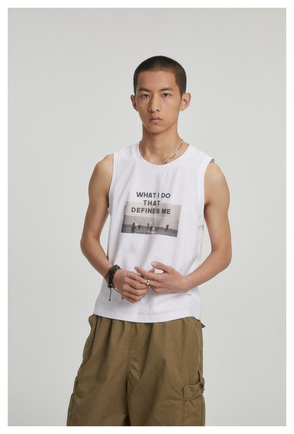 Close view of a model wearing a white sleeveless shirt with a text-and-beach-photo graphic and olive cargo pants.