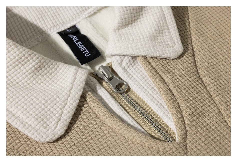 Close-up of a beige textured jacket with a white collar, metal zipper, and sewn-in black label.
