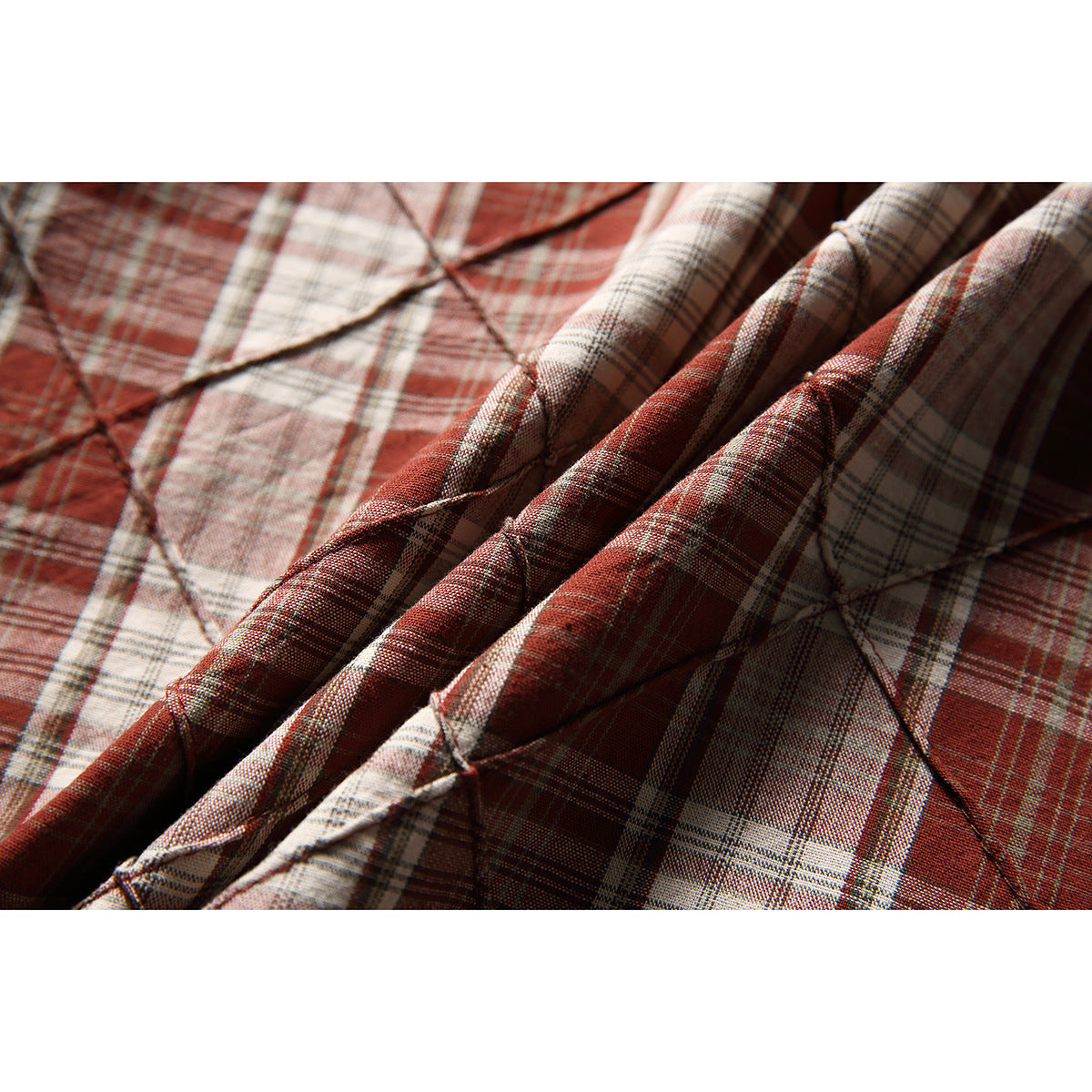 Close-up showing the shirt’s rust, cream, and gray plaid fabric and raised diamond-pattern stitching.