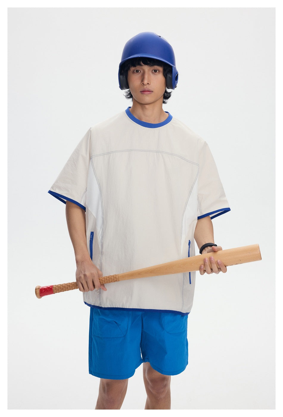 Front view of a model wearing an oversized cream shirt with blue trim, bright blue shorts, and a blue helmet.