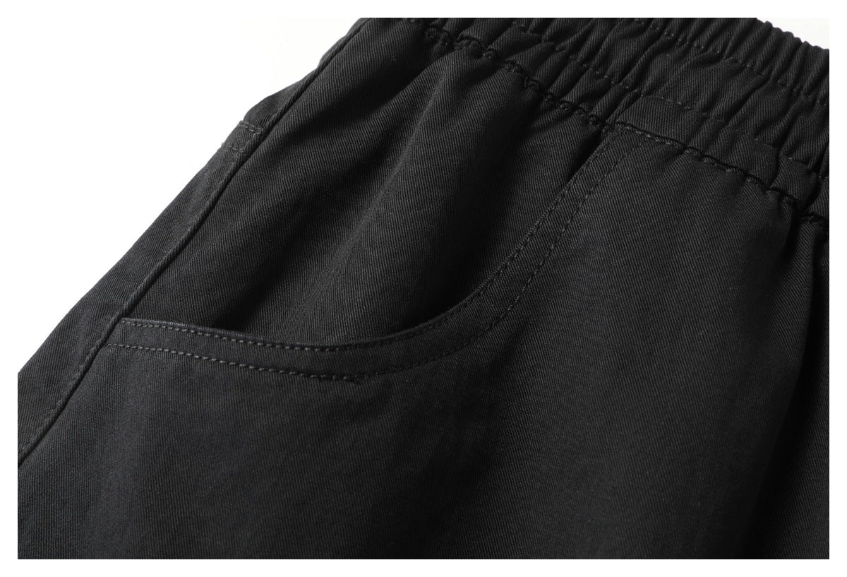 Close-up of a curved front pocket and stitching on black pants beneath the elastic waistband.