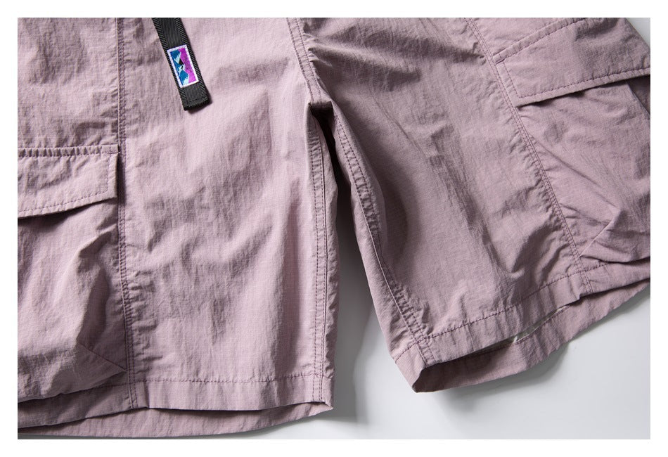 Close-up of pale mauve cargo shorts showing the leg seams, flap pocket, hem, and a small colorful fabric tab.