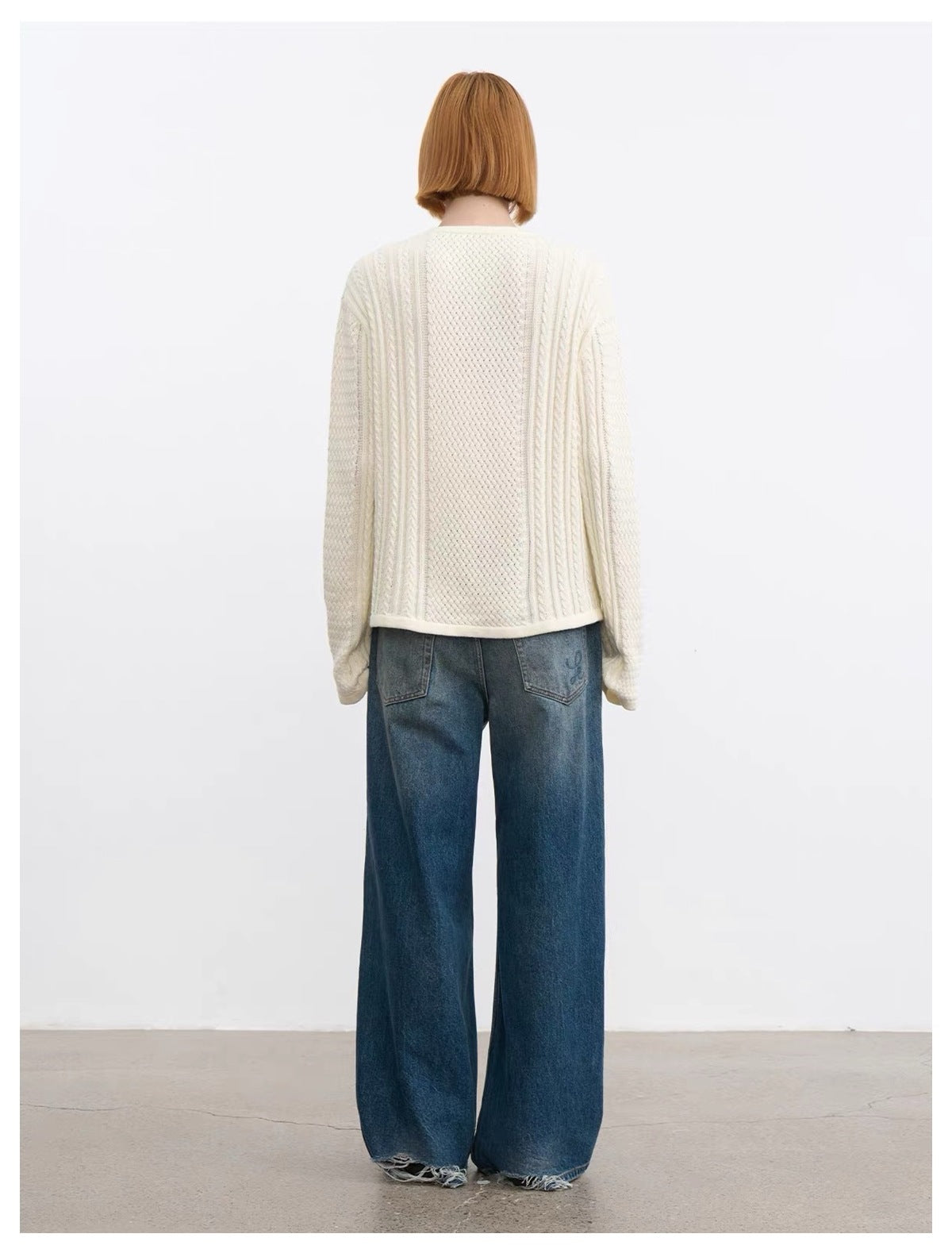 Rear view of a model wearing a cream cable-knit sweater and wide-leg blue jeans.