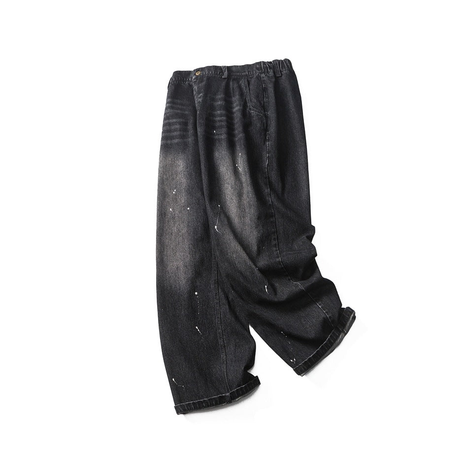 Full view of loose black washed trousers with a button waist, front pockets, white paint splatters, and rolled hems.