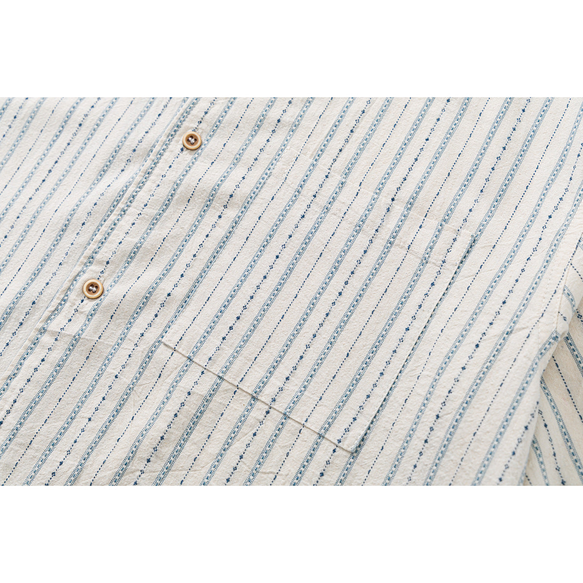 Close-up of a cream shirt's blue patterned vertical stripes, tan buttons and front chest pocket.
