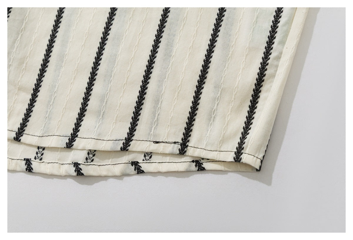 Close-up of the ivory shirt's lower hem with black braided vertical stripes and raised stitched lines.