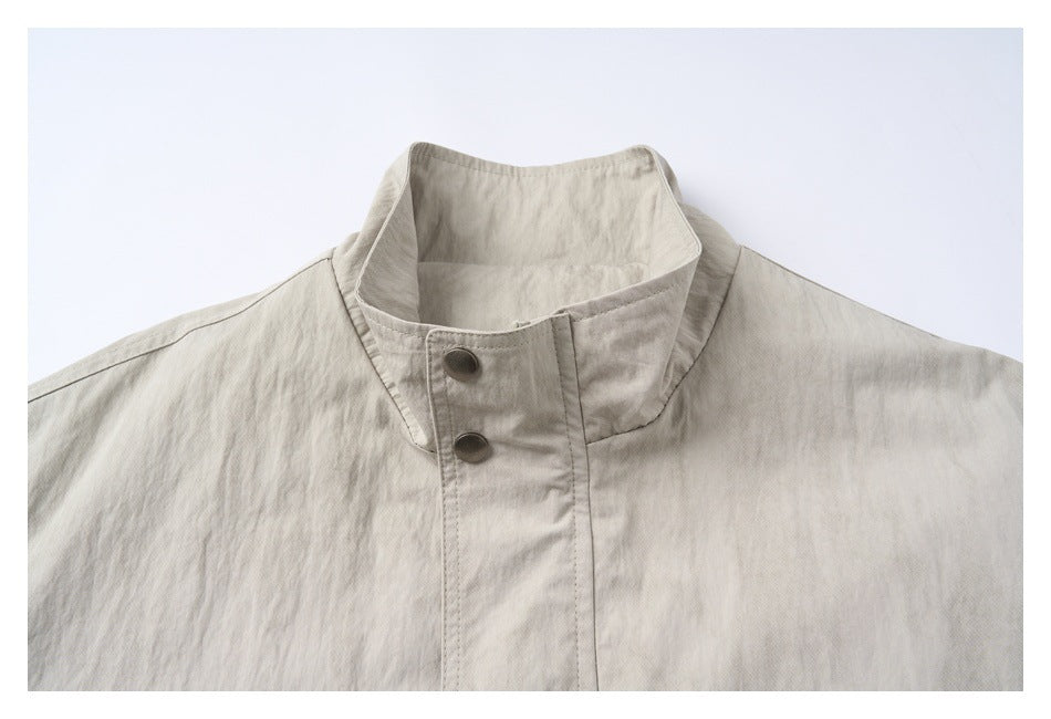 Close-up of the light gray-beige jacket's tall stand collar and two dark metal snap buttons.