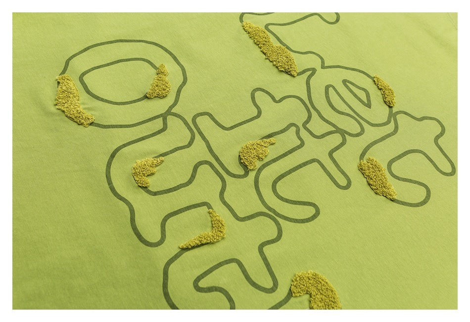 Close-up of a lime-green shirt with dark abstract line art and raised yellow embroidered accents.