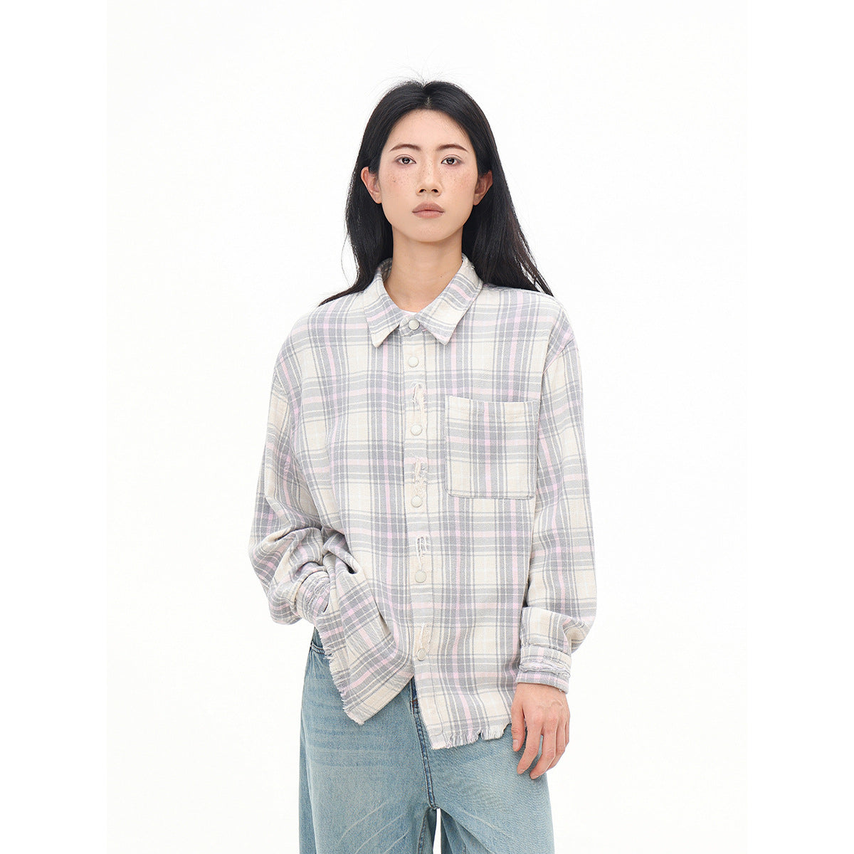 Closer view of a model wearing a muted pastel plaid button-up shirt with a chest pocket and frayed hem.