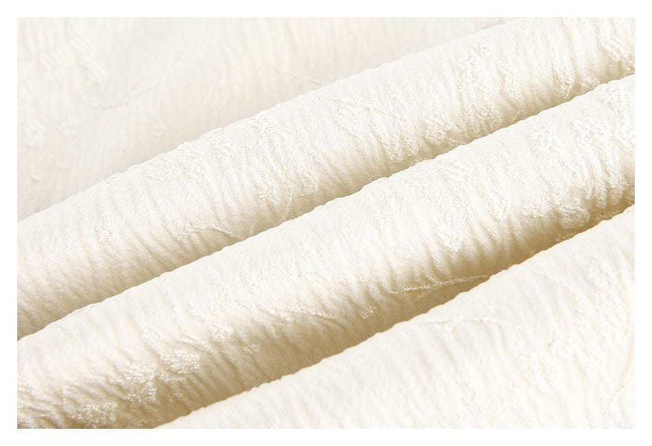 Macro view of ivory garment fabric with a raised, irregular textured pattern.