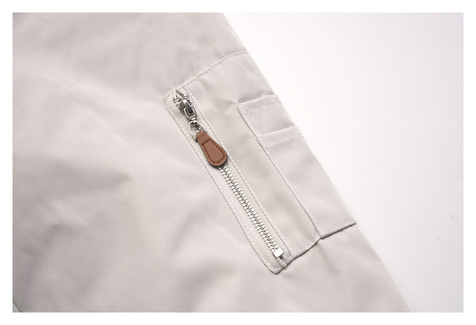 Close-up of a pale gray jacket sleeve with a silver zip pocket and brown pull tab.
