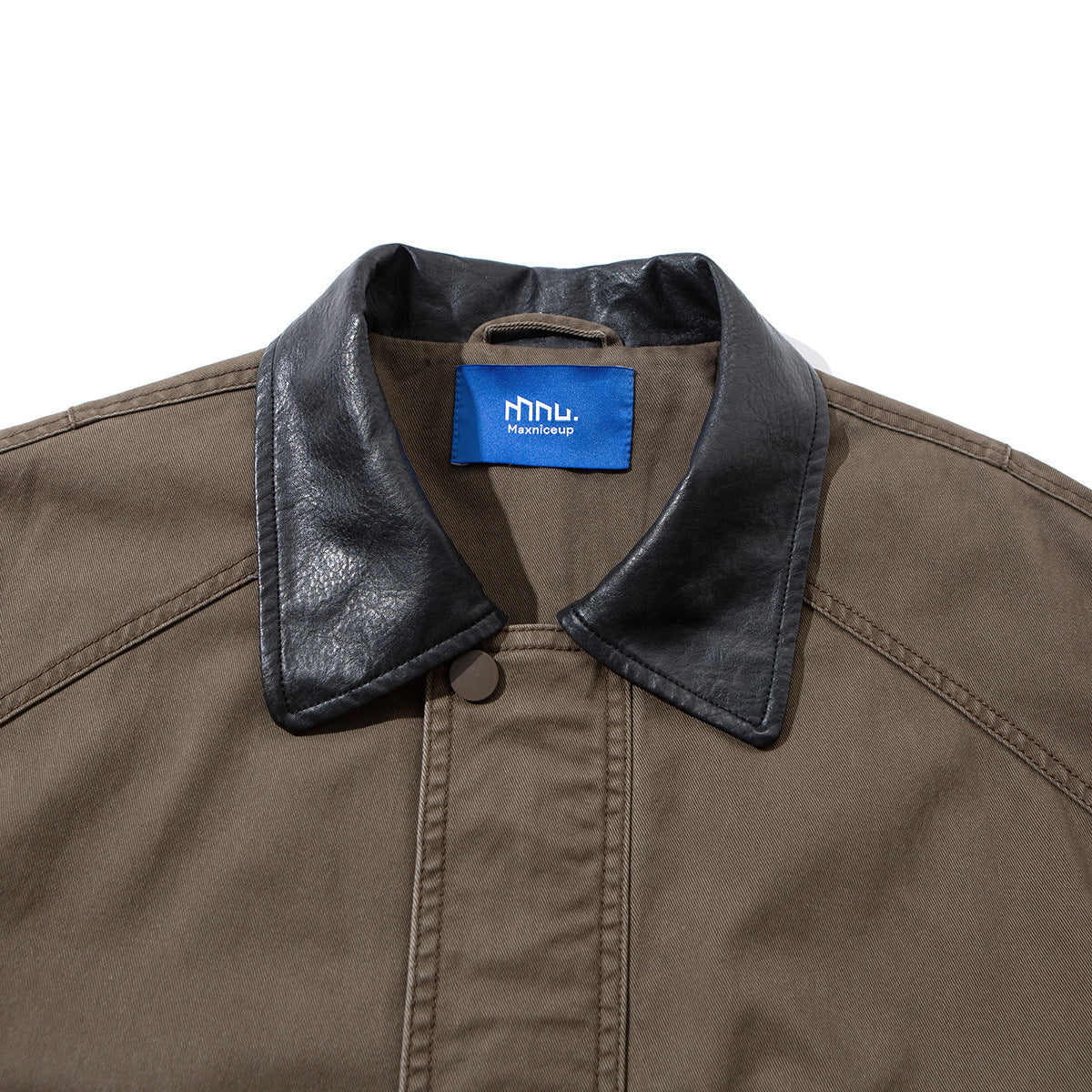 Close-up of a taupe jacket’s black leather-look collar, front placket, button, and blue neck label.