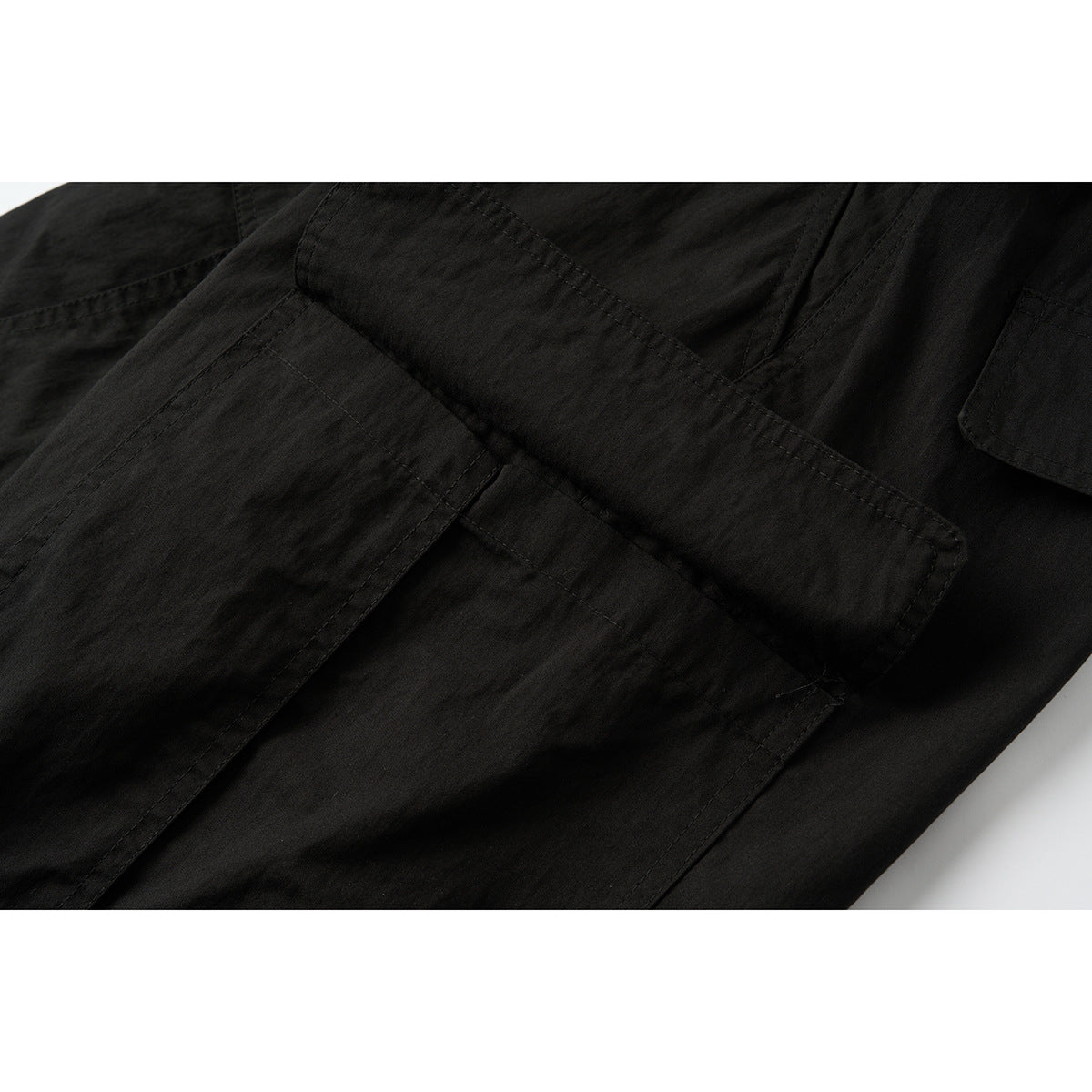 Close-up of black cargo pants with a large flap pocket and visible panel stitching.