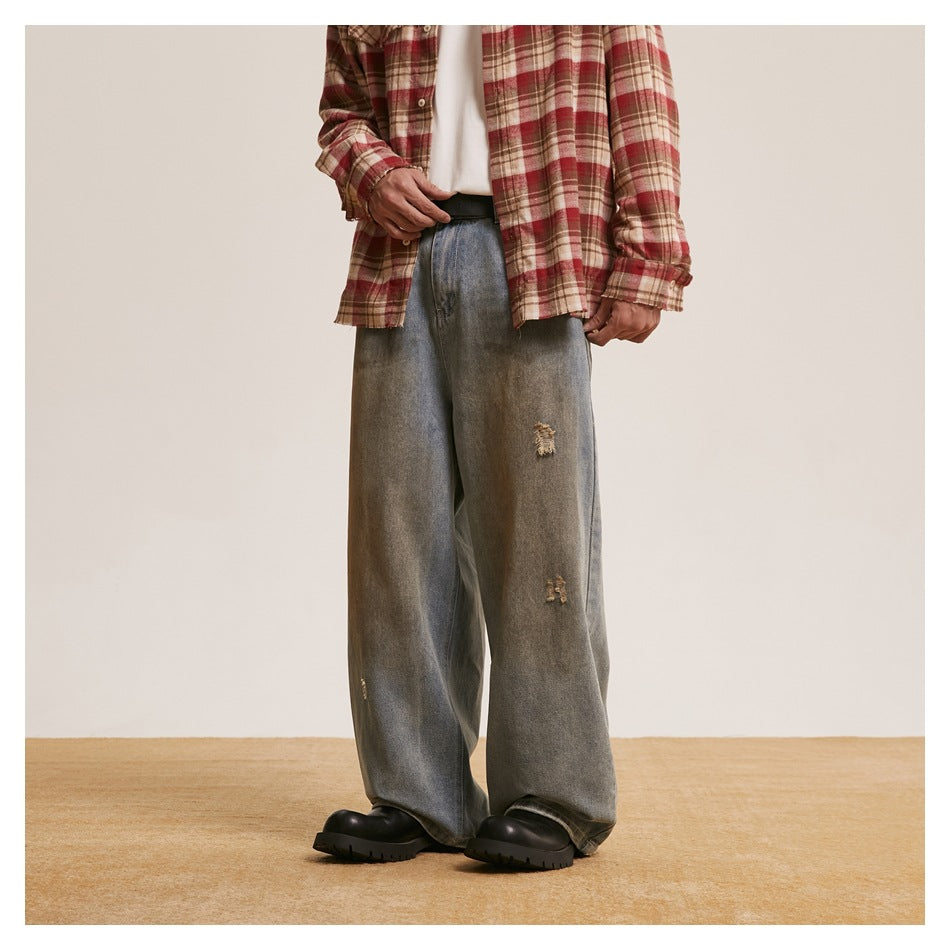 Front view of a model wearing loose, faded gray-blue jeans with distressed patches and black chunky shoes.
