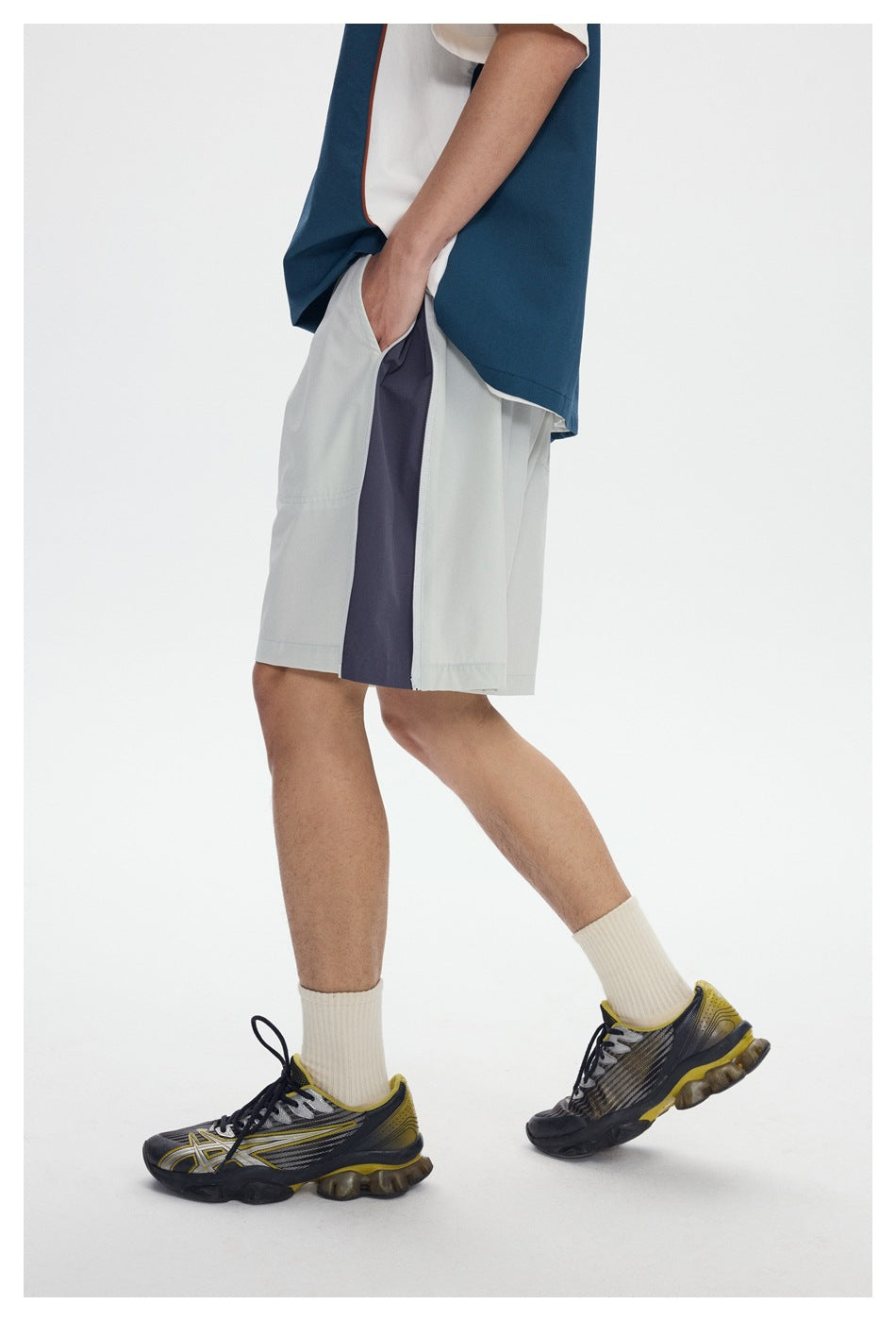 Side view of a model wearing light gray shorts with a dark gray side panel, hand in pocket, with sneakers