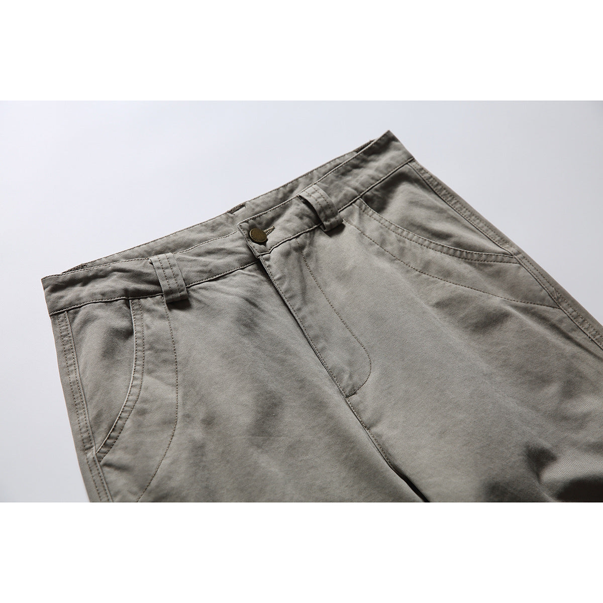 Close-up of gray work pants showing the waistband, button, belt loops, fly, and front pockets.