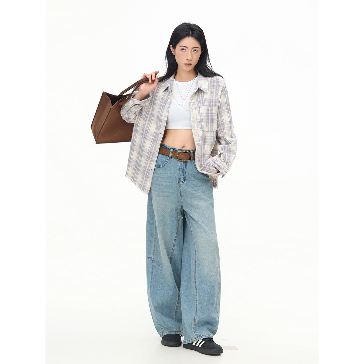 Model wearing an open muted pastel plaid shirt over a white crop top with wide-leg blue jeans.