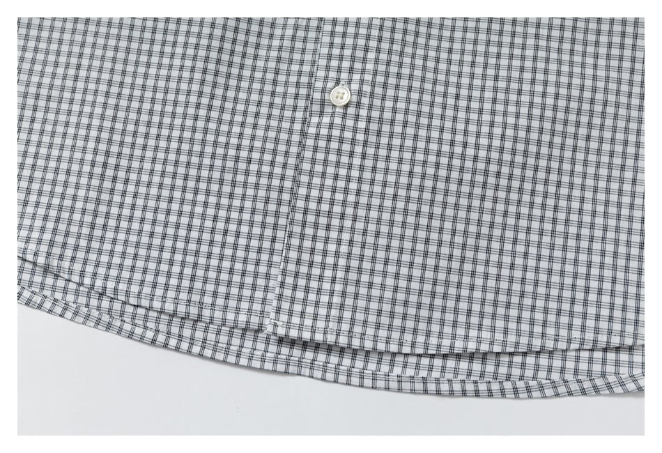 Close-up of a black-and-gray checked shirt showing a white button, front placket and curved hem.