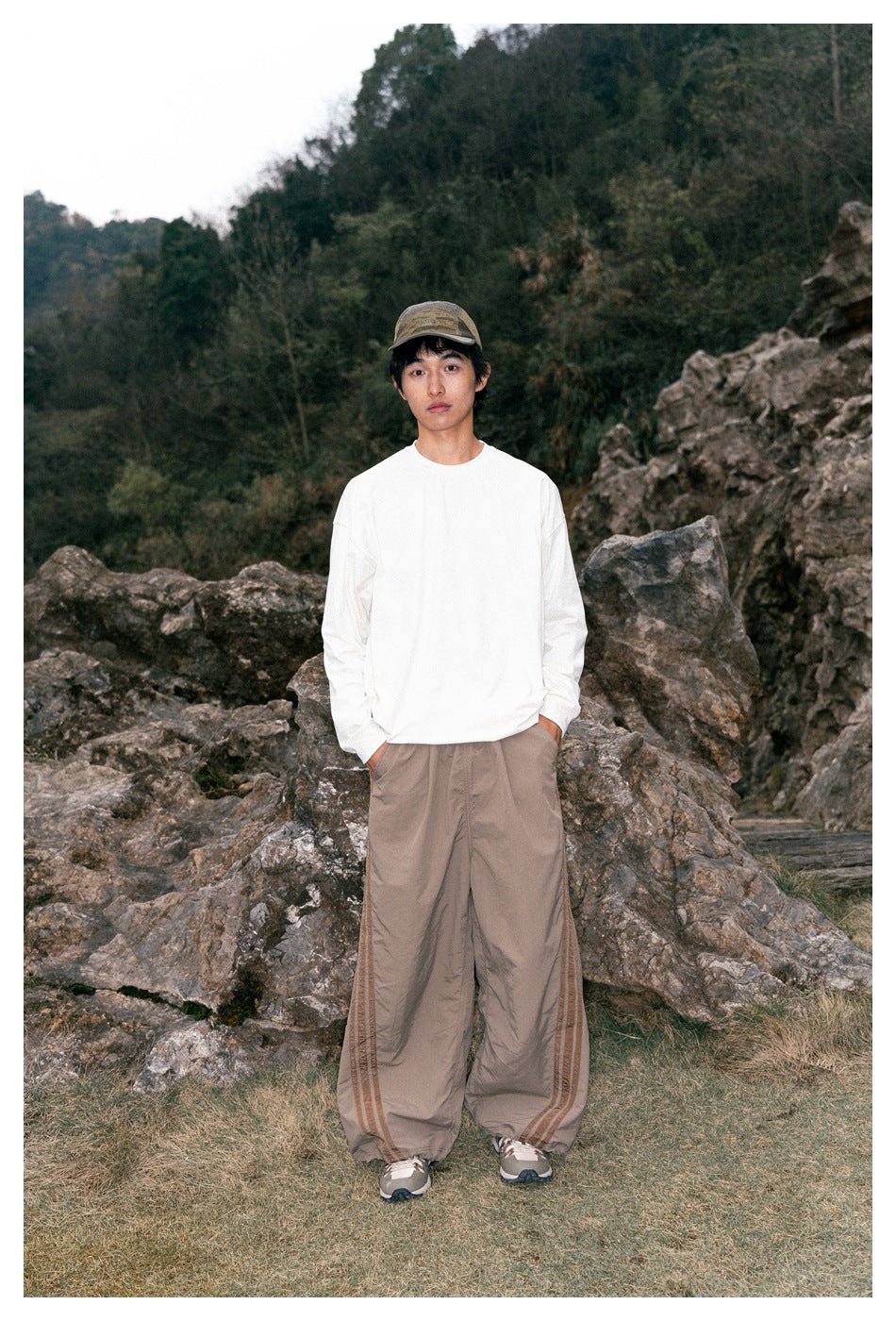 Front view of a model wearing a white long-sleeve shirt and loose taupe pants with brown side stripes.