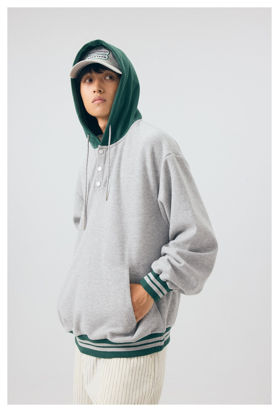 Three-quarter view of a model wearing a light gray hoodie with a dark green hood and striped cuffs and hem.