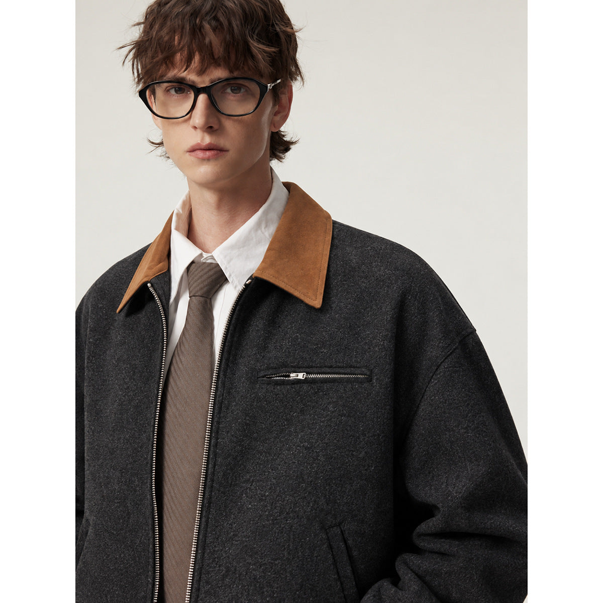 Close-up front view of a model wearing a charcoal jacket with a tan pointed collar and zippered chest pocket.