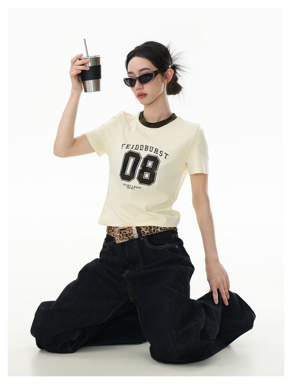 Model kneeling in an ivory graphic T-shirt and dark wide-leg jeans, holding a tumbler; front view.