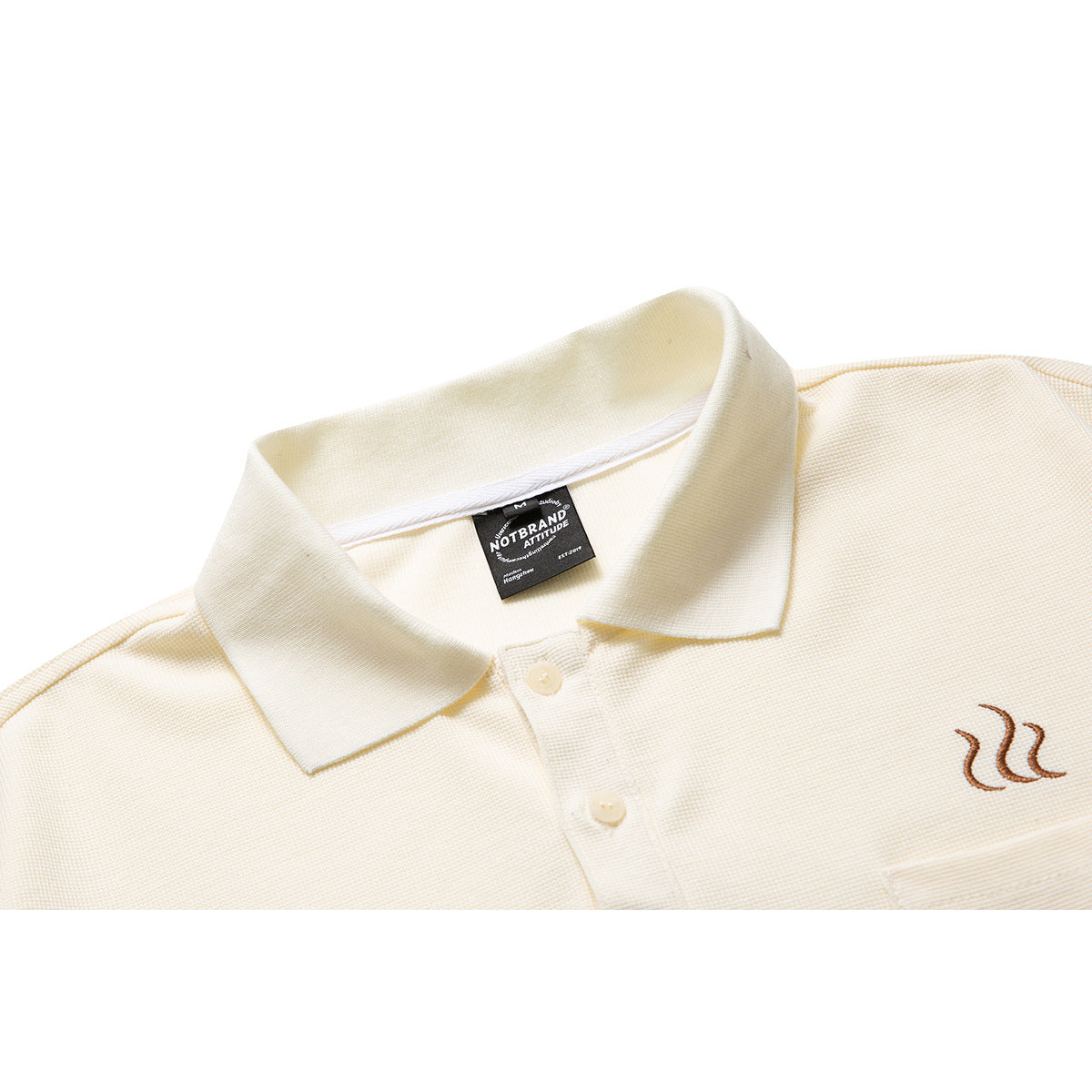Close-up of an ivory polo shirt collar, button placket, and small brown embroidered chest motif.