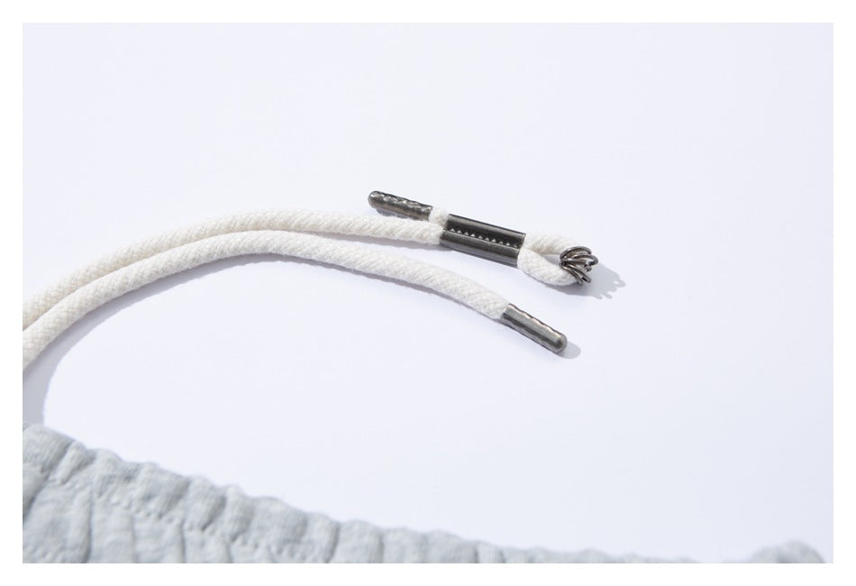 Close-up of white sweatpants drawstrings with metal tips and a metal cord lock.
