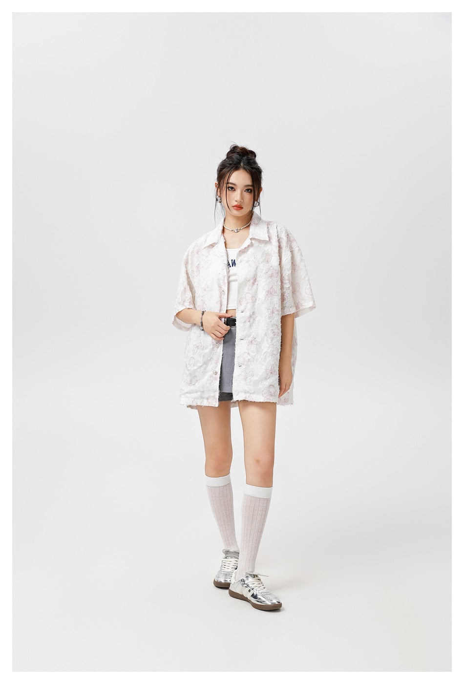 Model wearing an open white short-sleeve shirt with pale pink floral texture over a white tank, gray shorts and socks