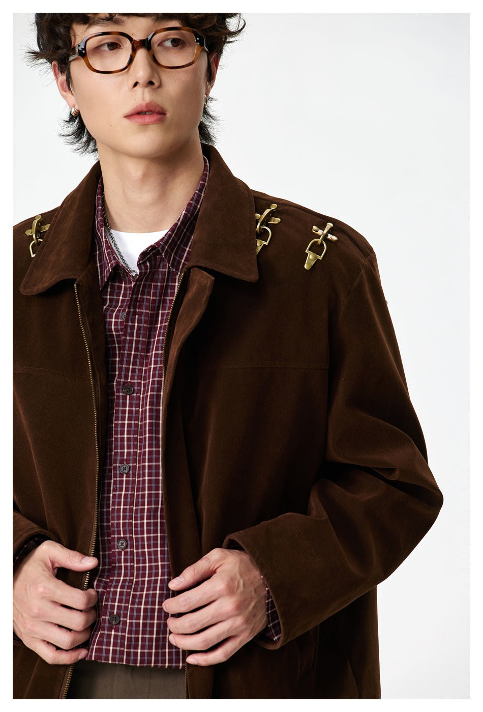 Close-up of a man in a brown zip jacket with gold shoulder hooks over a burgundy plaid shirt