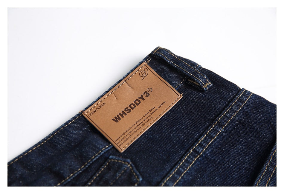 Close-up of dark indigo jeans waistband with a tan leather label and contrasting golden stitching.