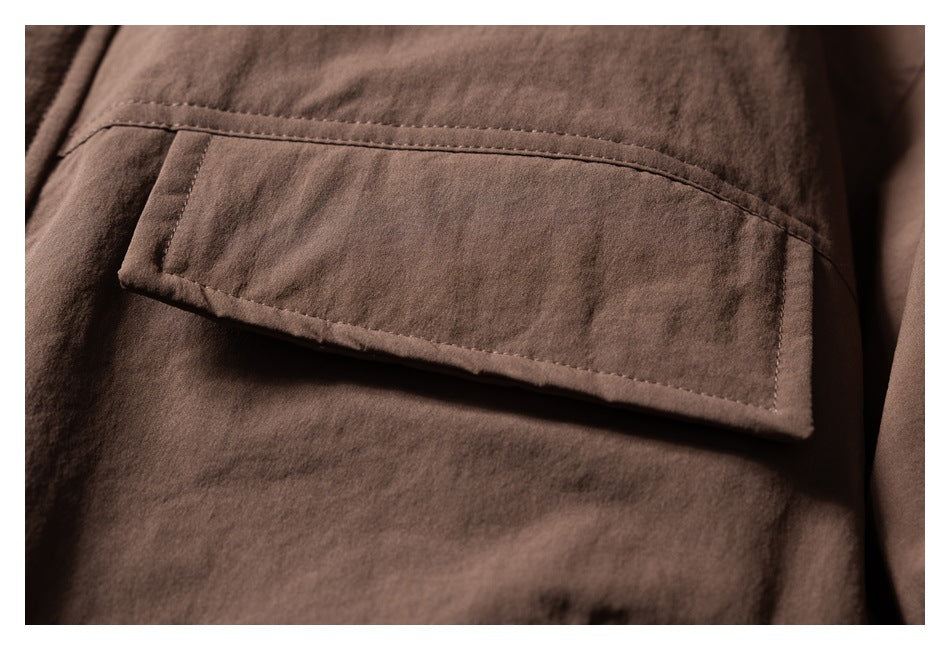 Close-up of a stitched rectangular flap pocket on brown jacket fabric.