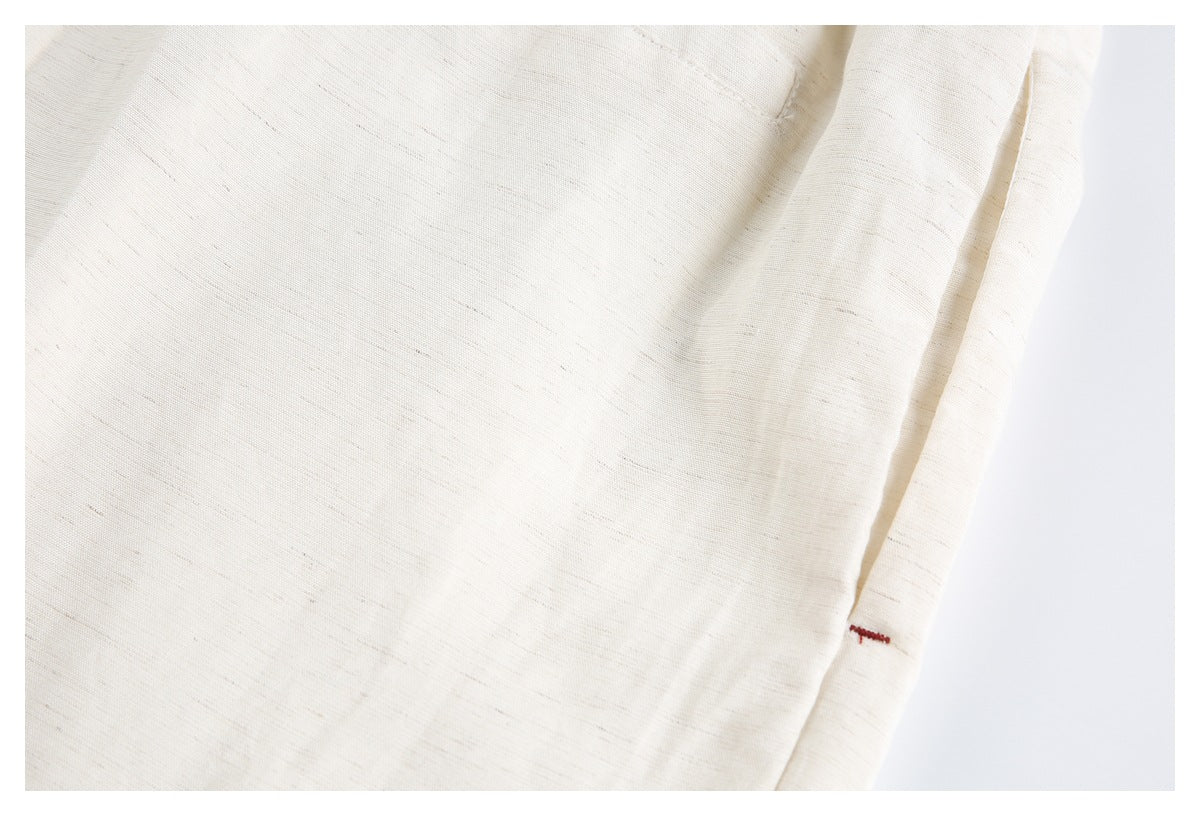 Close-up of cream trouser fabric and a seam with a small red stitched accent.