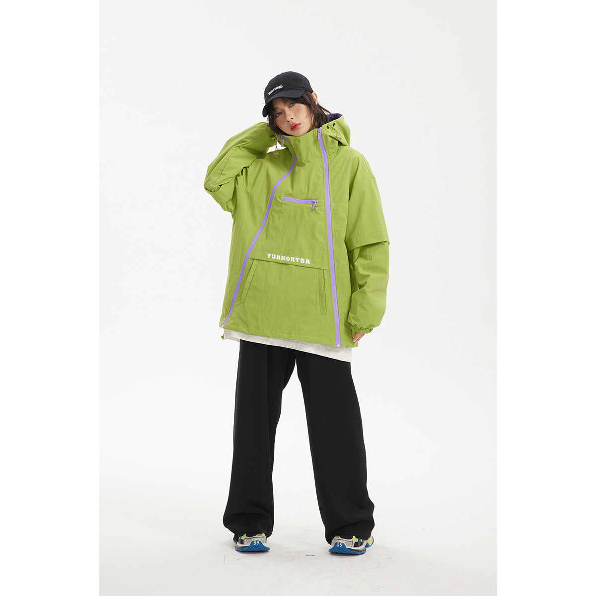 Model wearing a lime green hooded jacket with lavender zippers and a large front pocket, paired with black pants.