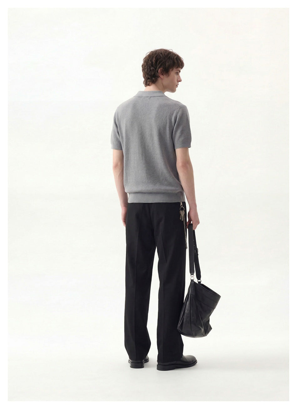 Back view of a model wearing a gray short-sleeve collared polo with a ribbed hem and black trousers.