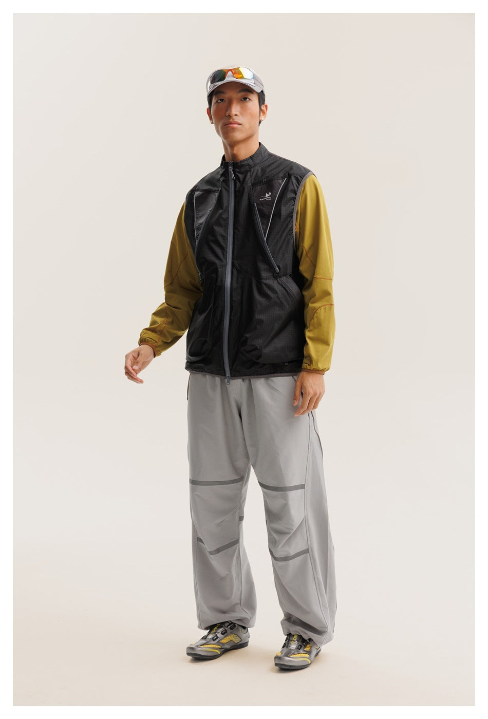 Front view of a model wearing a black zip vest over a mustard long-sleeve top and gray pants.