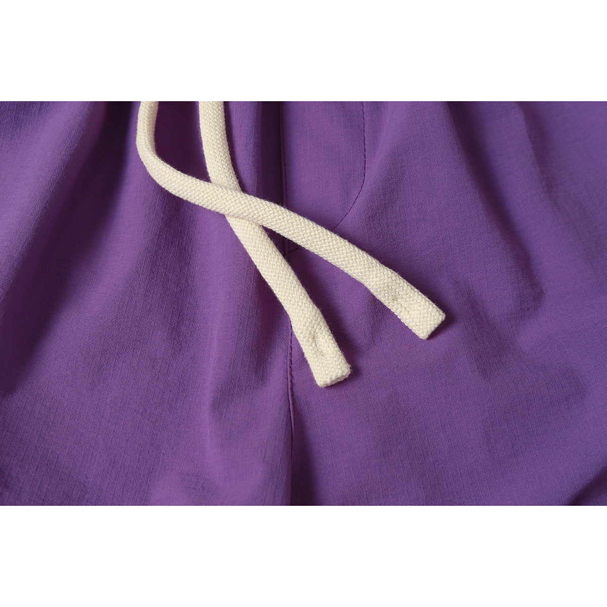 Close-up of purple pants with thick cream drawstrings and visible stitching.
