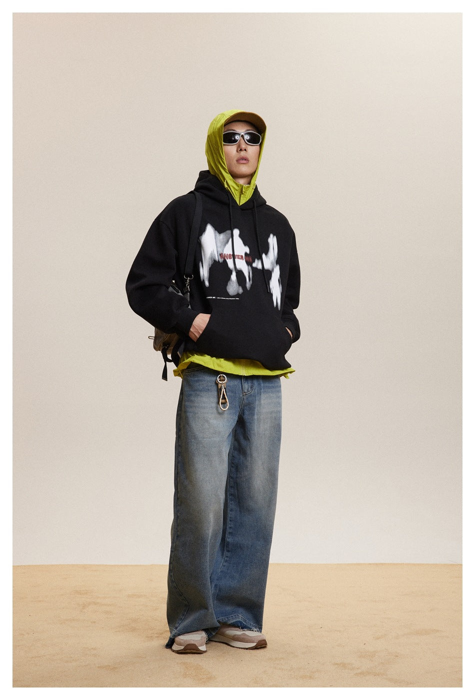 Full-length view of a person wearing a black graphic hoodie over a neon yellow hooded layer and wide blue jeans.