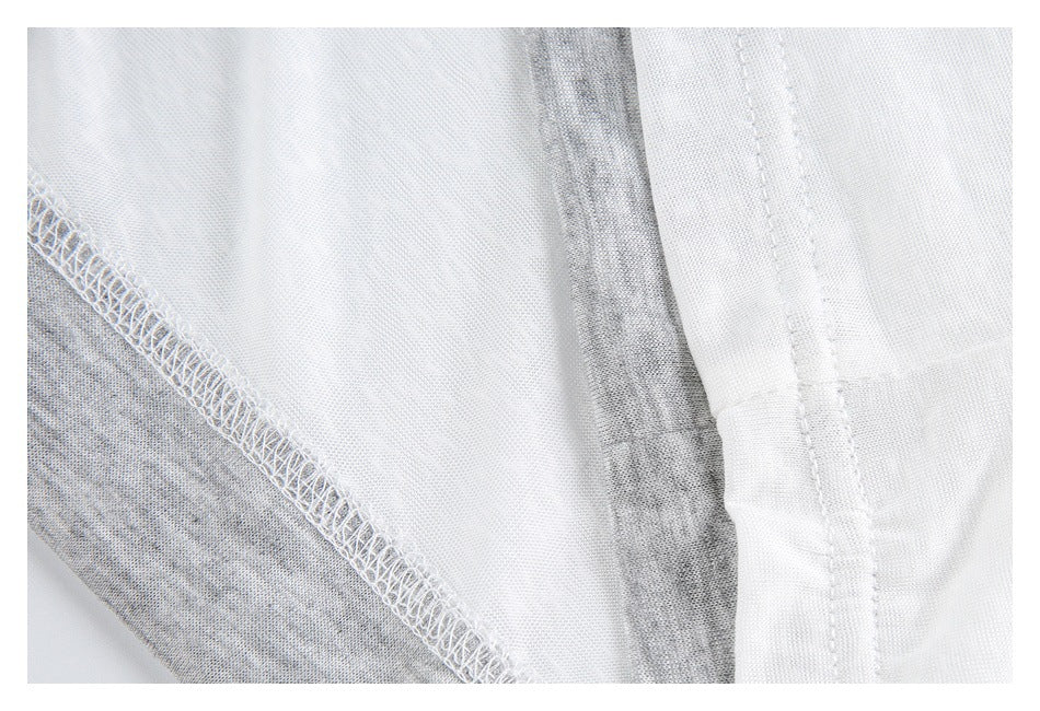Inside view of a white garment showing overlocked stitching and a folded seam with gray fabric beneath.