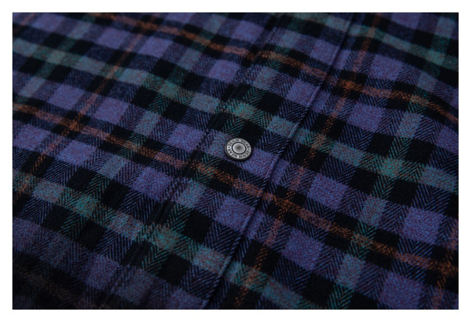 Close-up of a round metal button on purple, teal, and black plaid fabric.