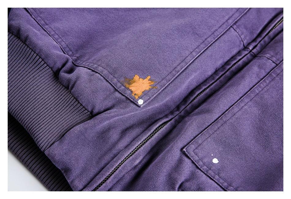 Purple jacket close-up showing a zipper, stitched pocket, ribbed hem, and orange and white paint-like marks.
