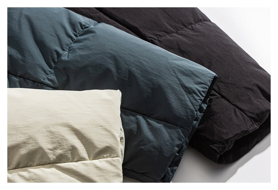 Padded jackets in dark blue-gray, black, and cream arranged overlapping on a white surface.