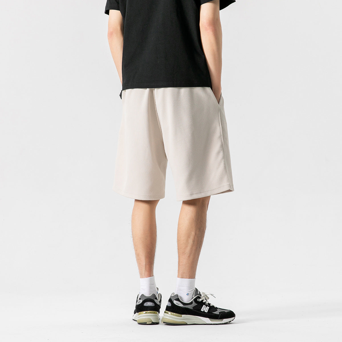 Rear view of a model wearing light beige knee-length shorts with a subtle vertical texture.