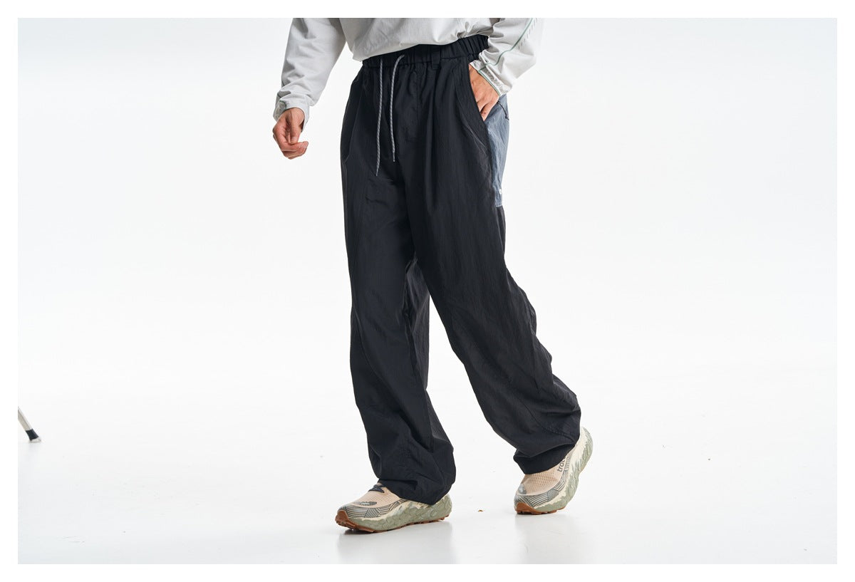 Model wearing loose black drawstring pants with a white top and patterned sneakers, shown at an angle.