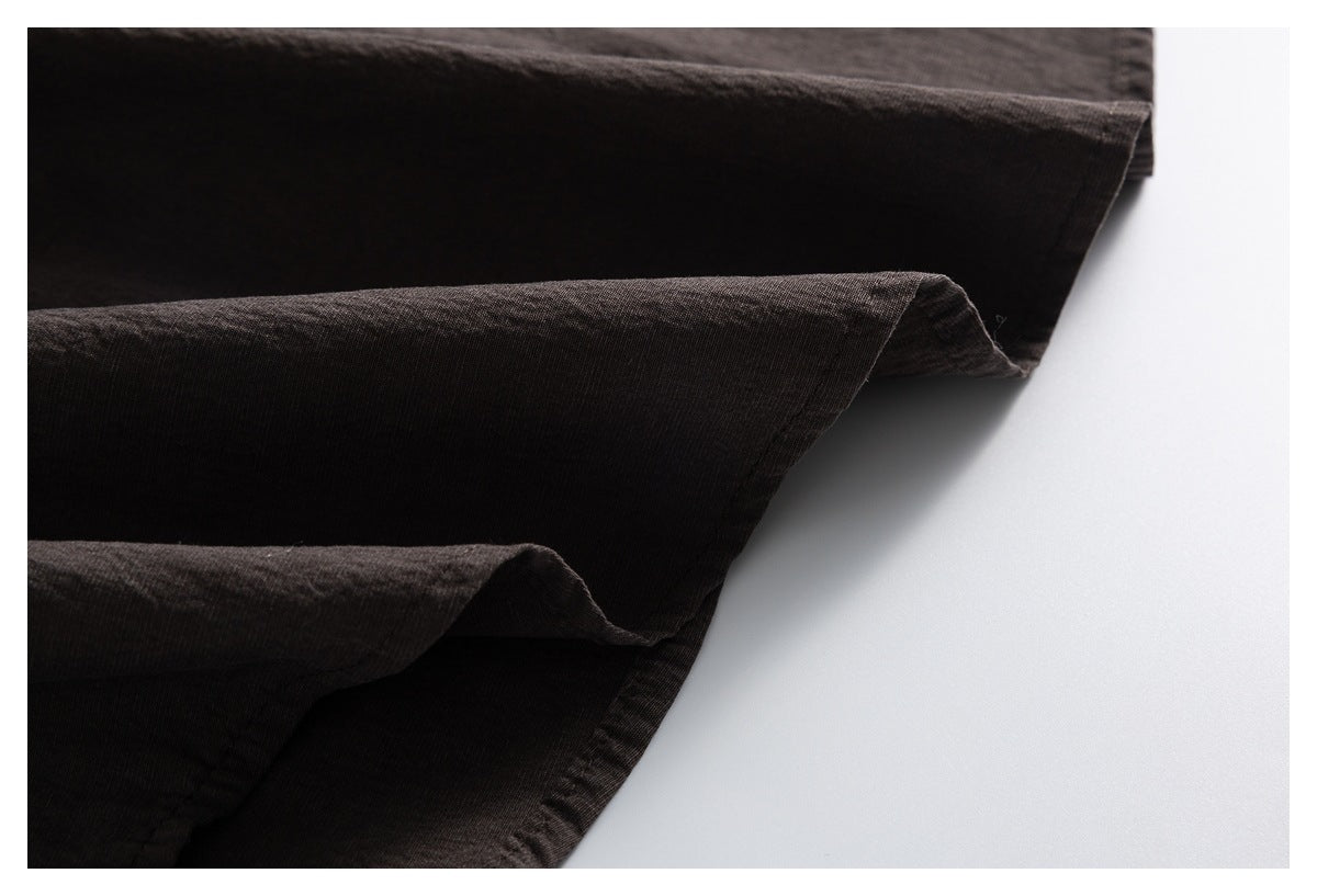 Close-up of dark charcoal-brown fabric folded in overlapping layers, showing a stitched edge.