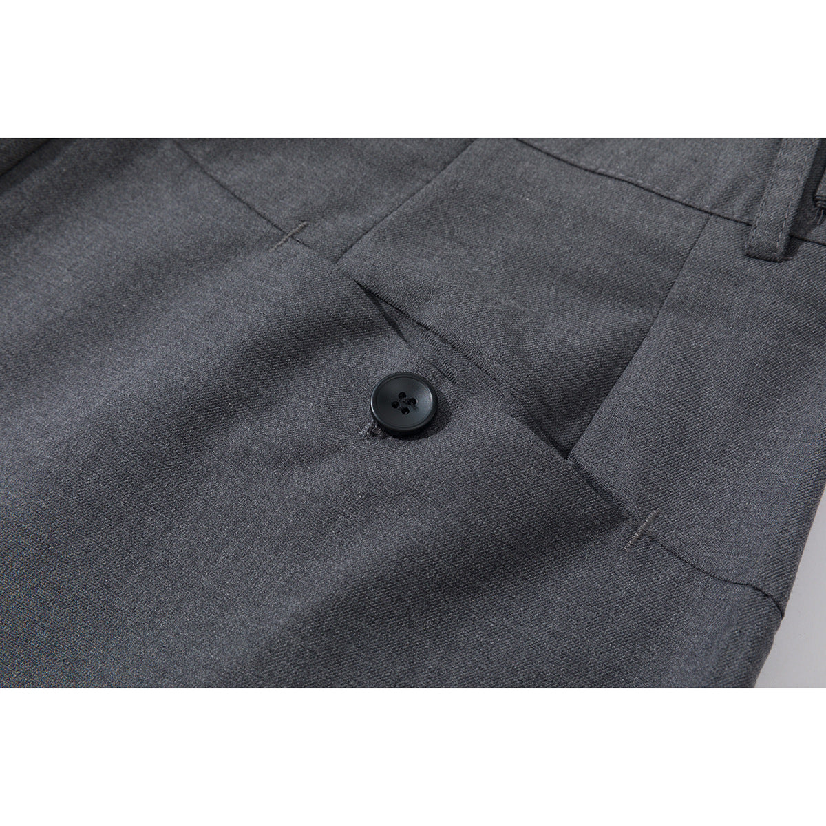 Close-up of charcoal gray trousers showing a black button, fabric texture, and stitched seams.