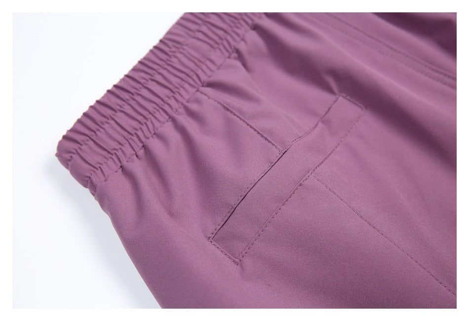 Close-up of purple trousers showing the gathered elastic waistband and a stitched pocket opening.