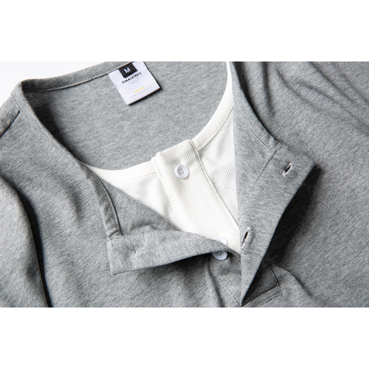 Close-up of a gray shirt's white-button placket, contrasting inner panel, and neck label.